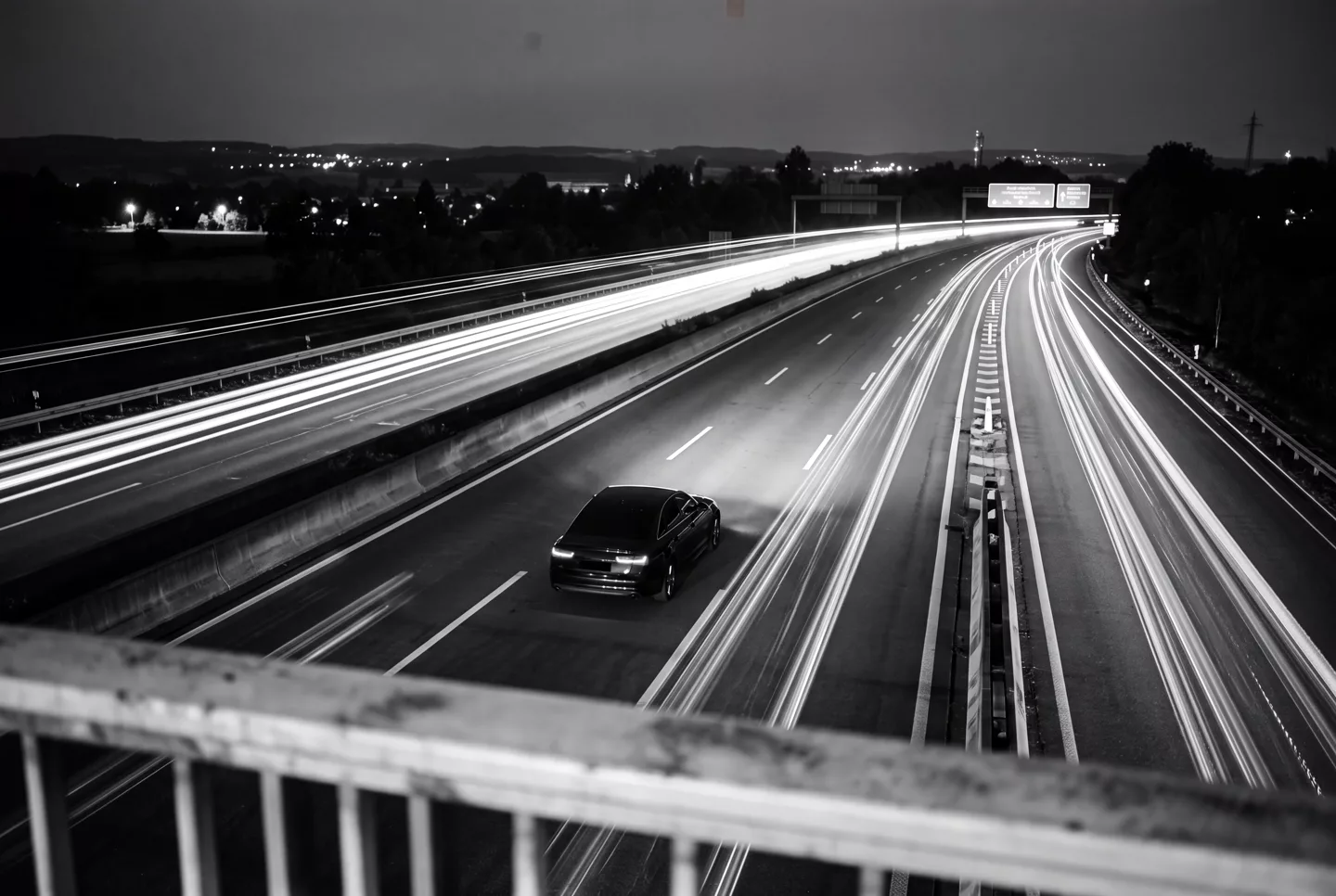 Lunga esposizione scenografica in bianco e nero: berlina di notte in autostrada, scie di luce sullo sfondo