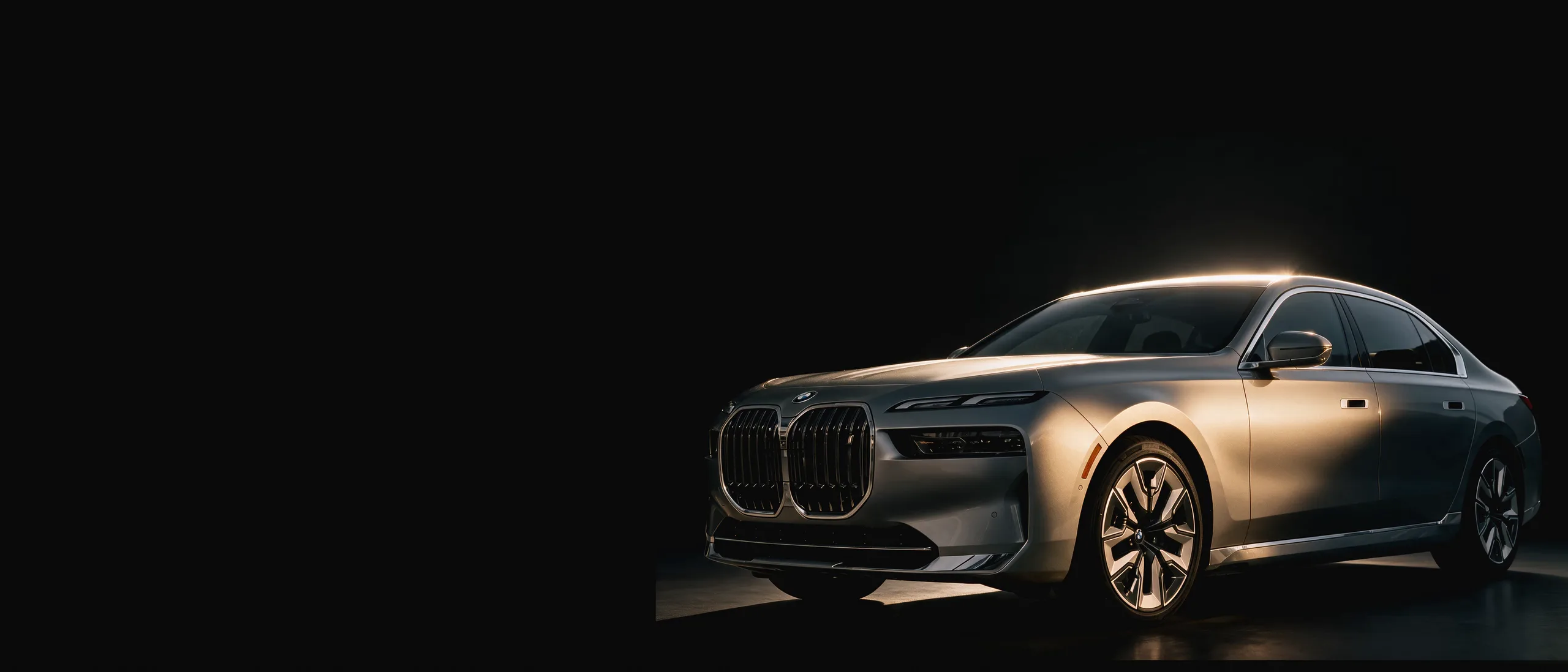 Inszenierte dunkle Studio-Bühne: eine silberne Limousine in Dreiviertel-Frontansicht, ein schmaler Messing-Lichtstreifen wandert über Dachlinie und Flanke.