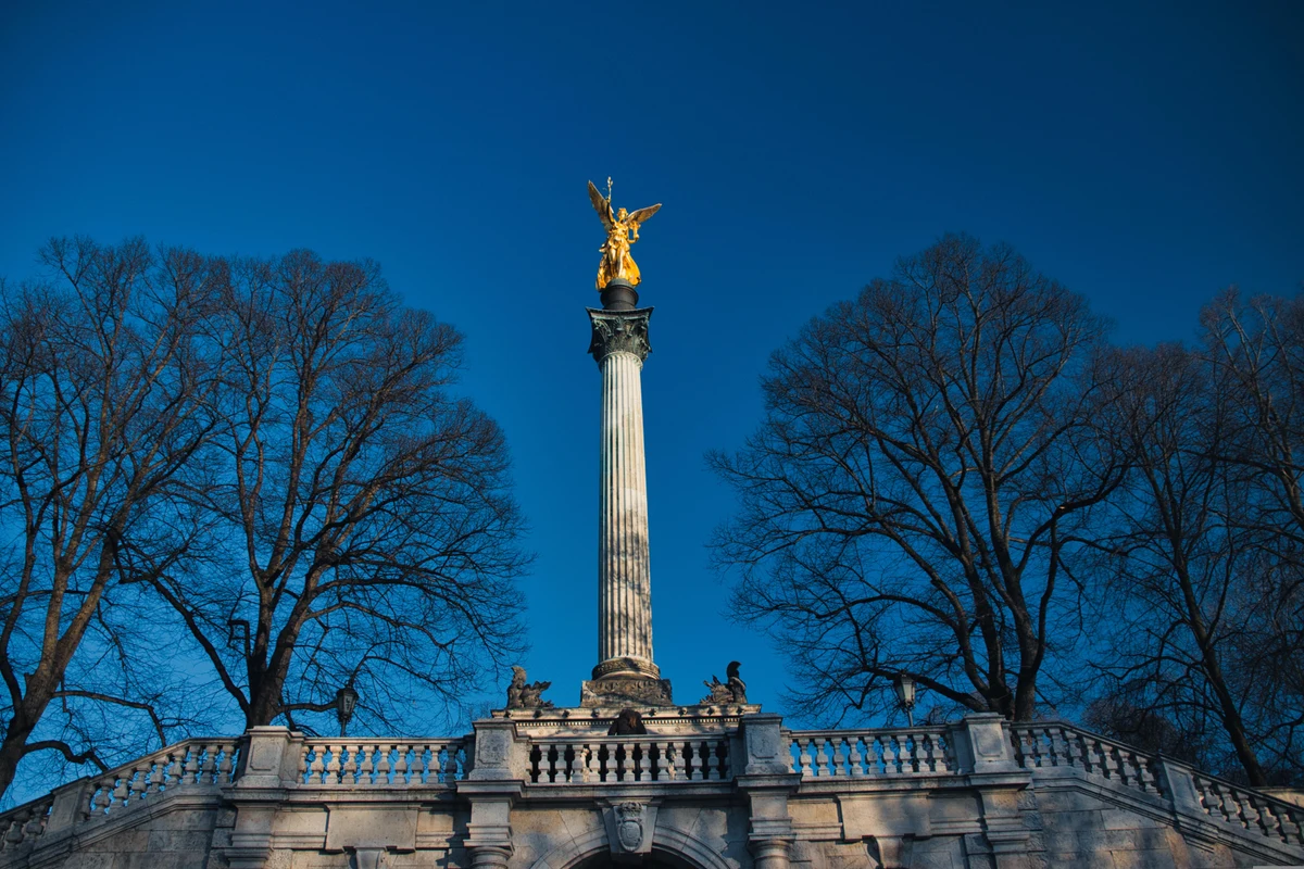 Friedensengel الذهبي فوق عموده في ميونخ، بين الأشجار.